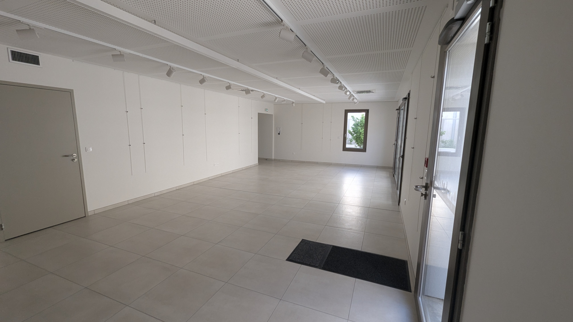 Salle vide avec porte, fenêtre, spots et tapis de sol.