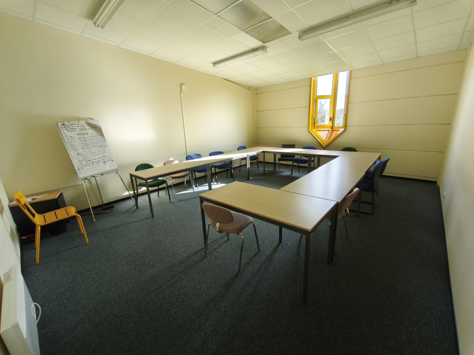 Salle avec tables, chaises, tableau blanc et fenêtre.