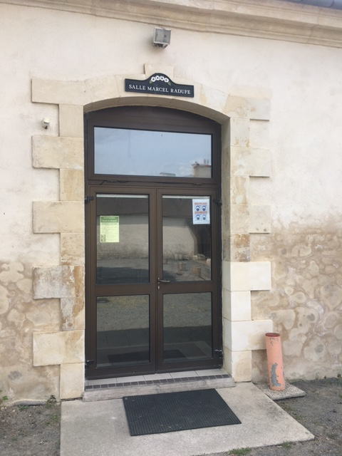 Entrée avec porte vitrée, paillasson, extincteur et enseigne.