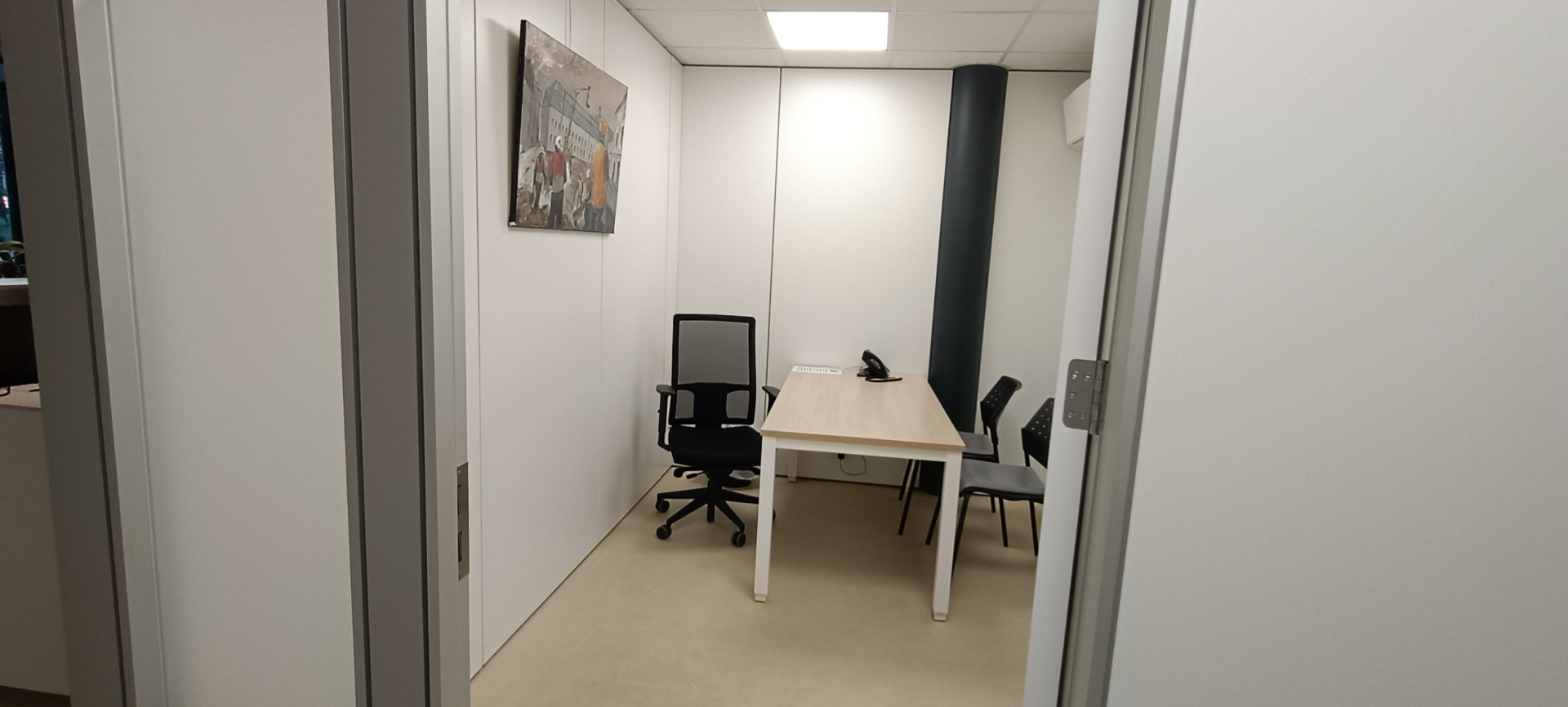 Petite salle de réunion avec table, chaises, téléphone et tableau.