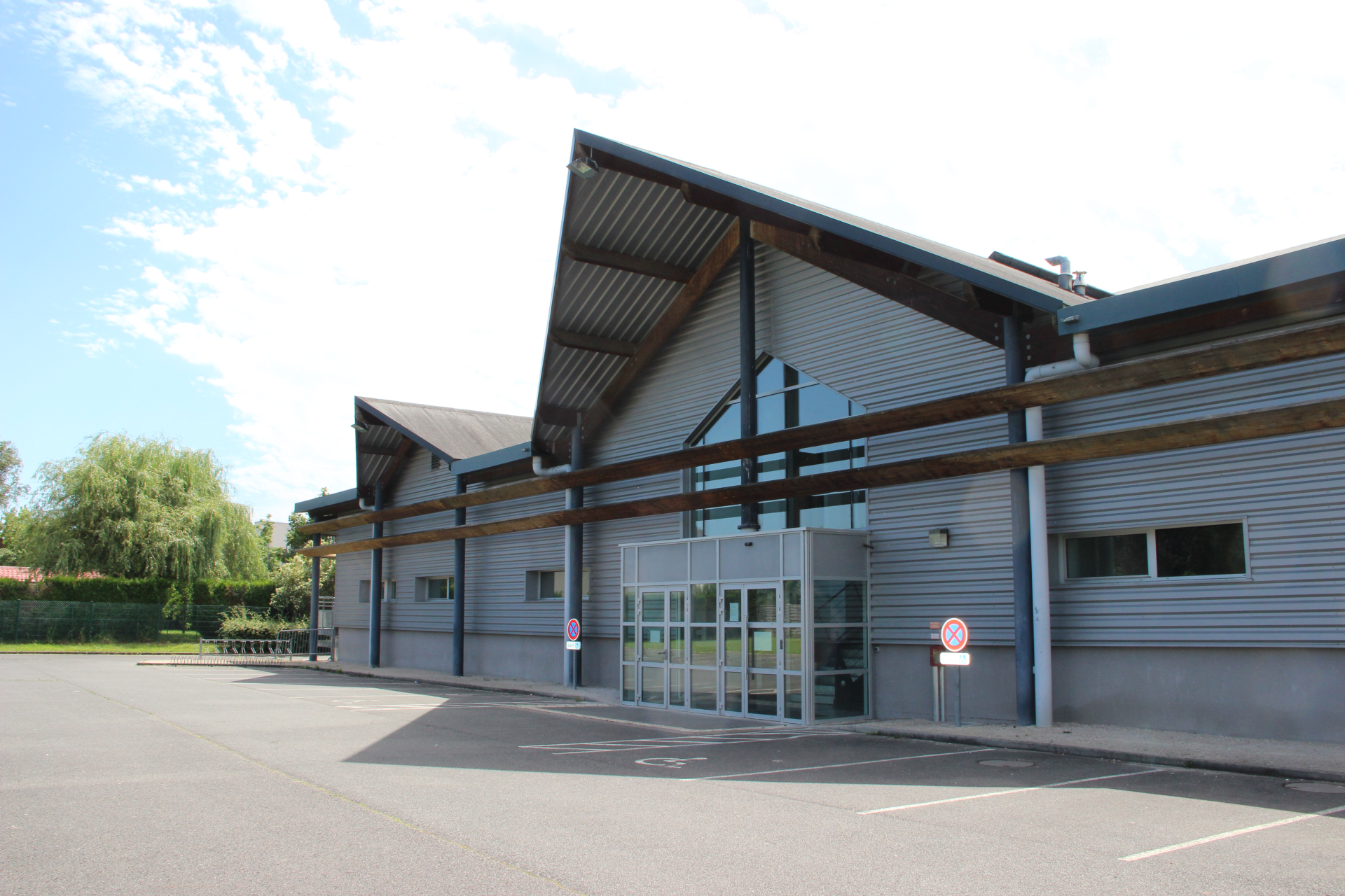 Bâtiment industriel avec entrée en verre, parking et arbre.