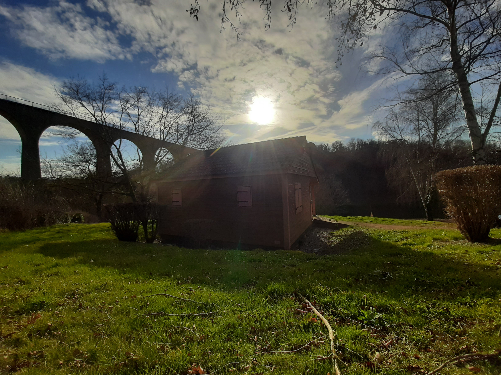 Cabane en bois près d'un pont ferroviaire sous un ciel partiellement nuageux.