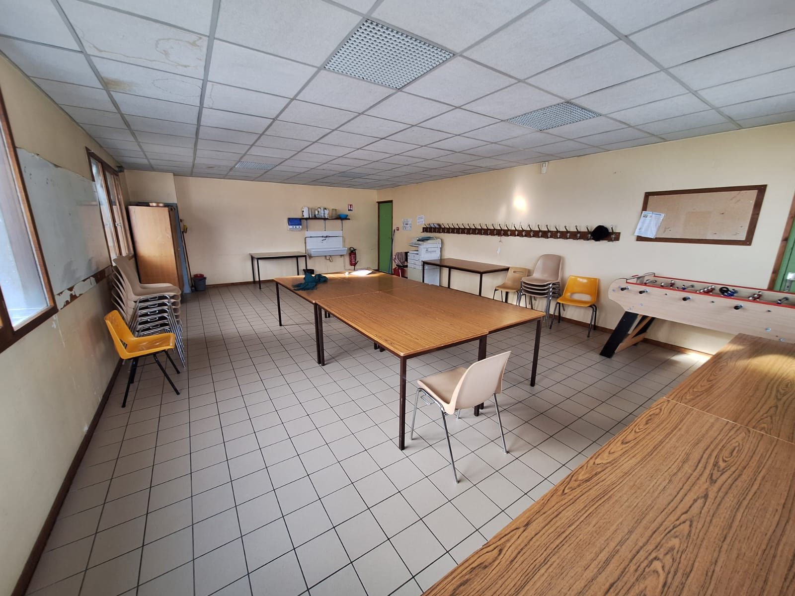 Salle avec tables, chaises, tableau, évier, frigo et machine à café.