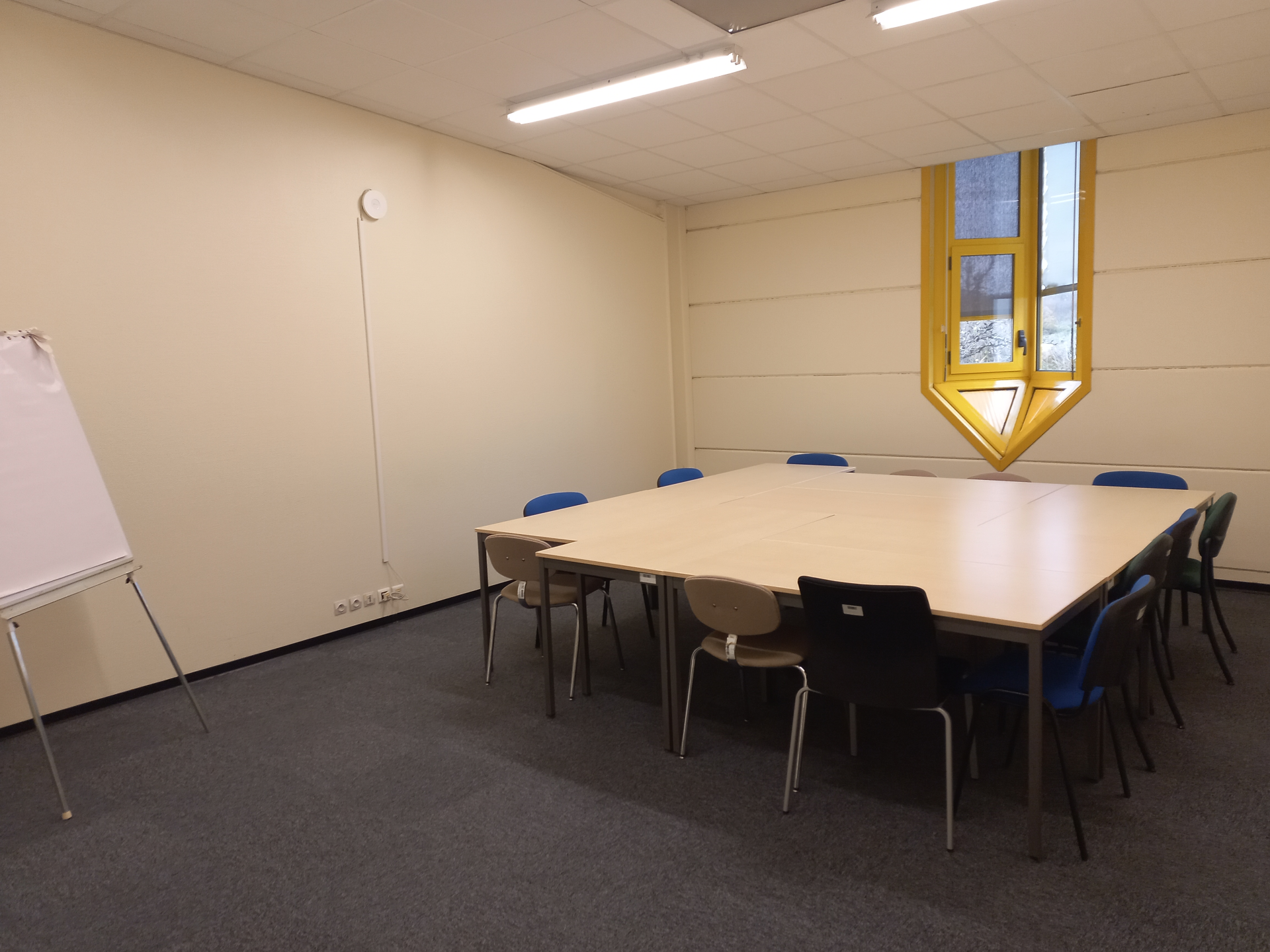 Salle de réunion avec table, chaises, tableau blanc et fenêtre.