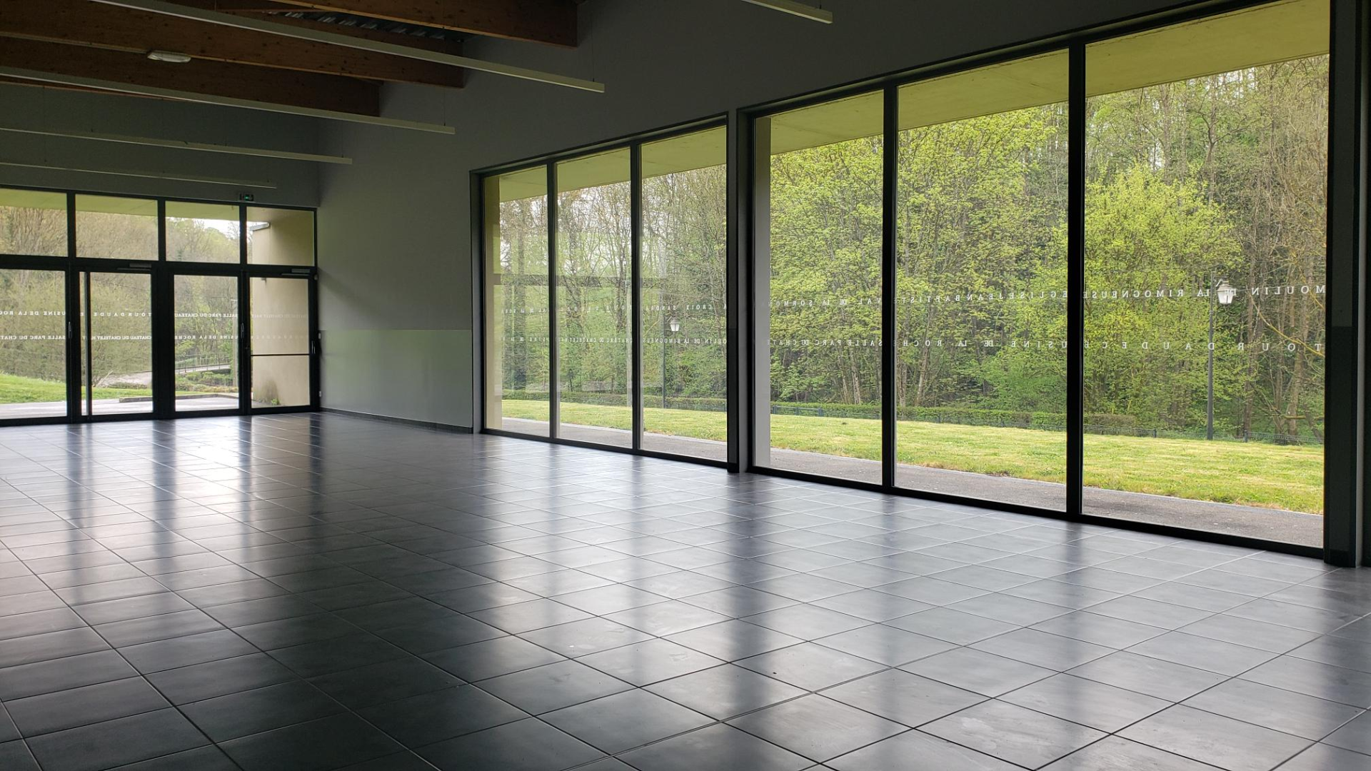 Salle vide avec grandes baies vitrées.