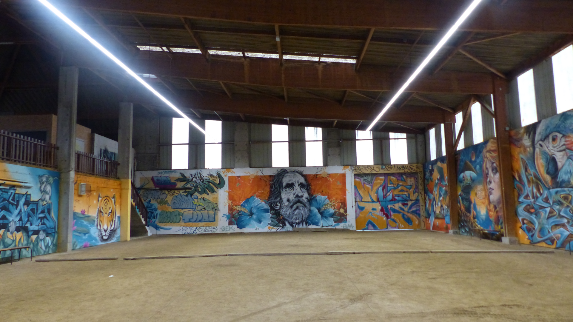 Atelier avec graffitis muraux, sol en béton, fenêtres et éclairage fluorescent.