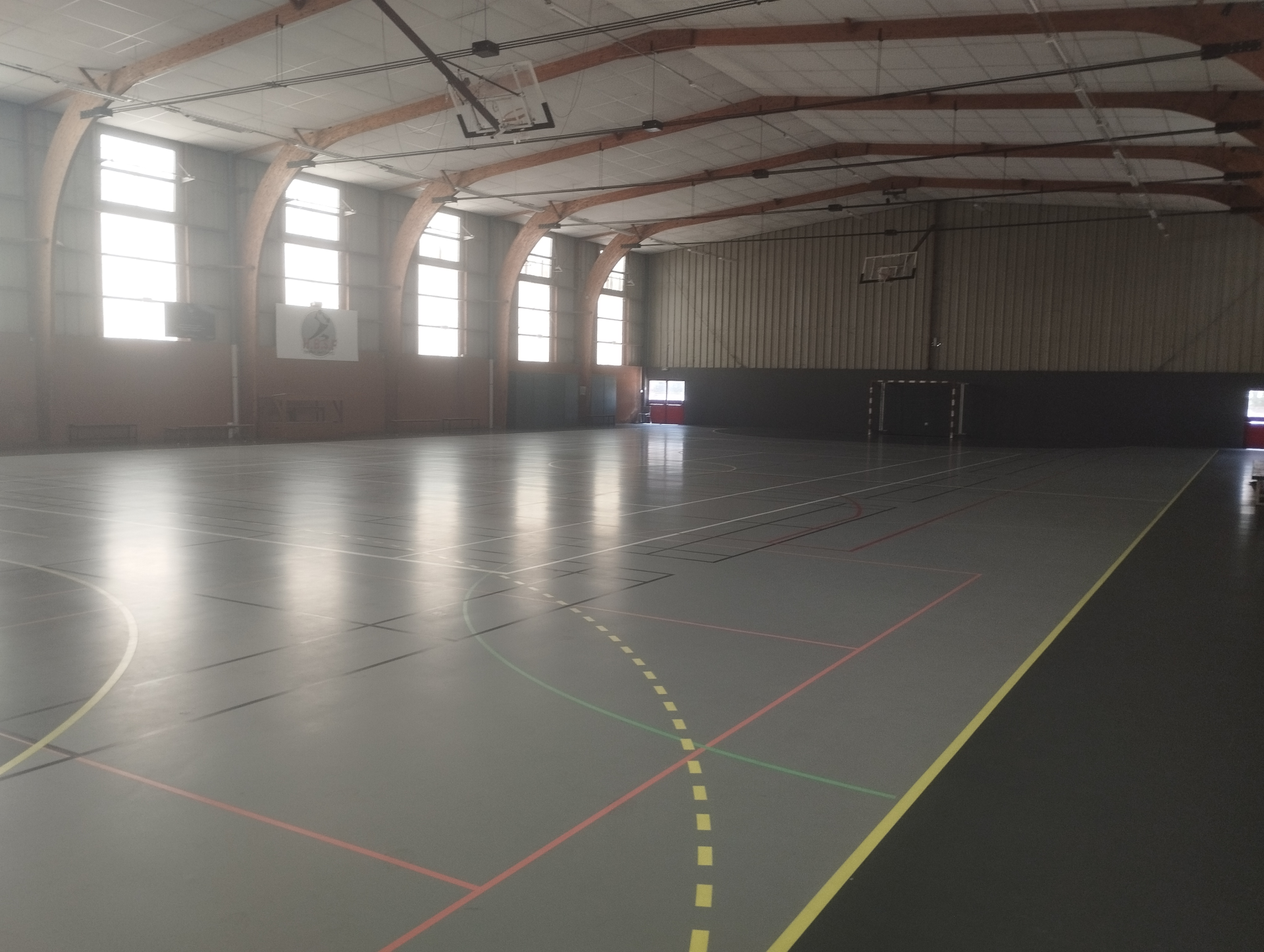 Salle de sport avec panier de basket, lignes de terrain et fenêtres.