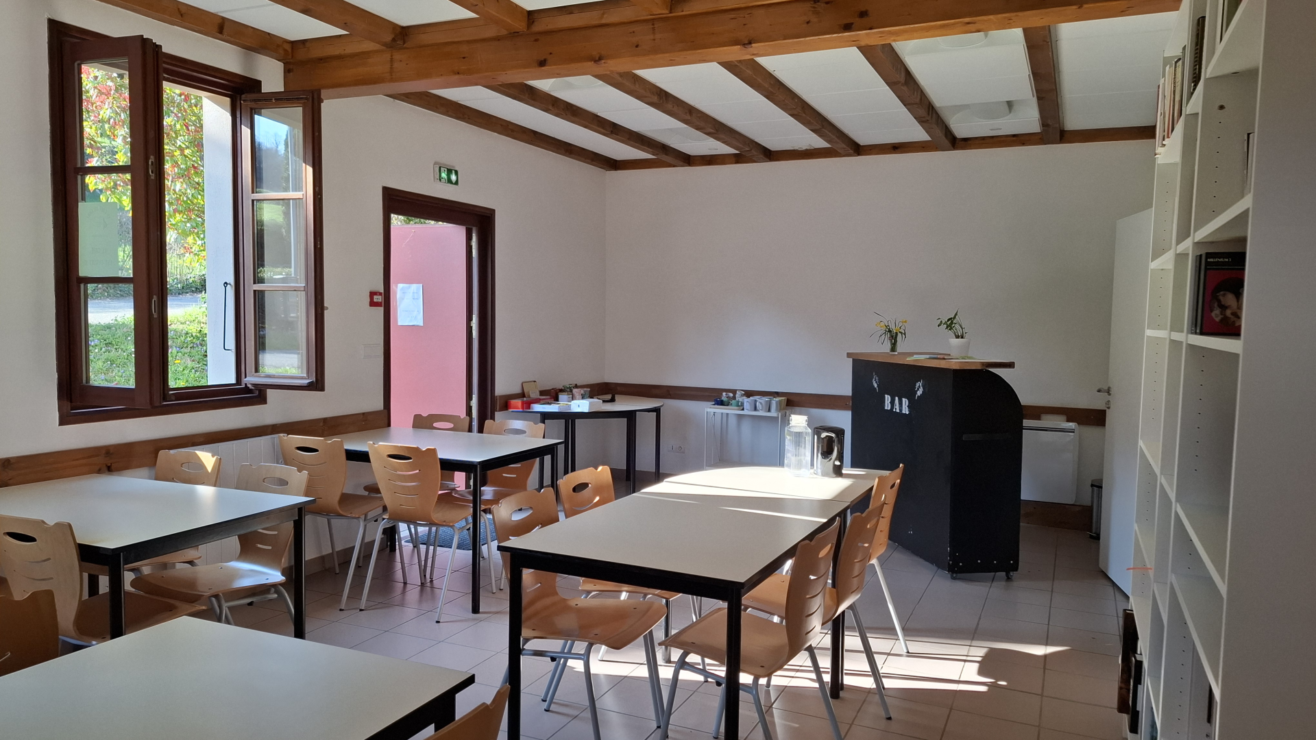 Salle avec tables, chaises, étagères, machine à café et plantes.