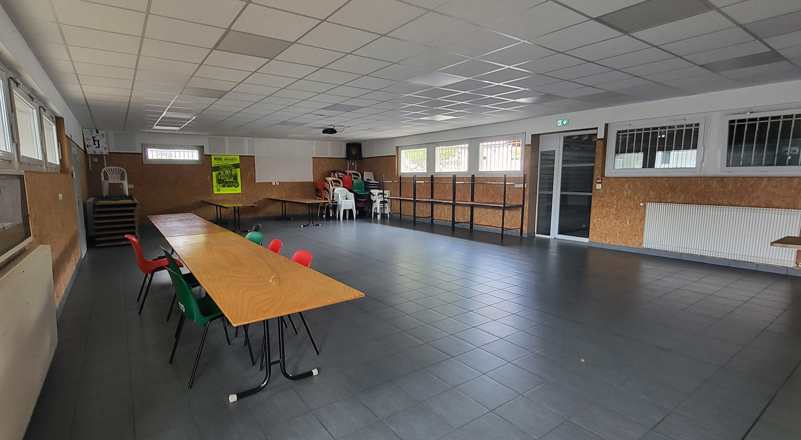 "Salle avec tables, chaises, radiateurs, placard, et affiche murale."