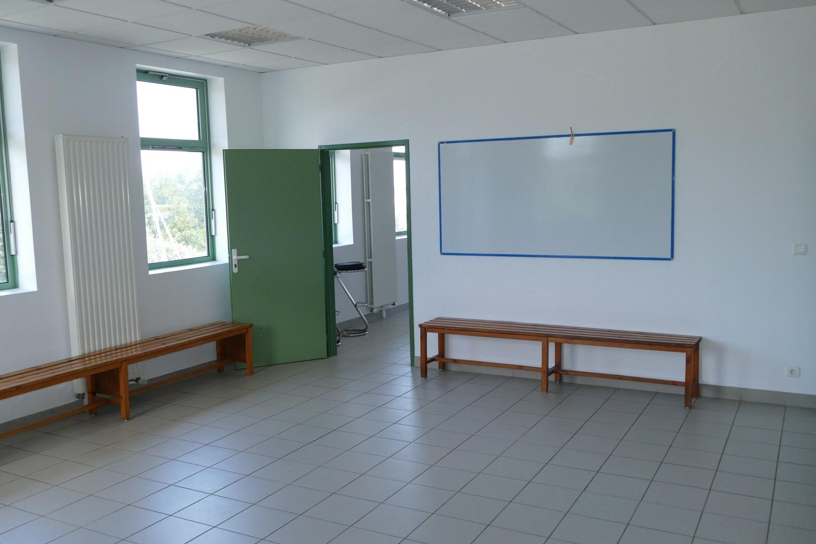 Salle avec bancs, tableau blanc et porte verte.