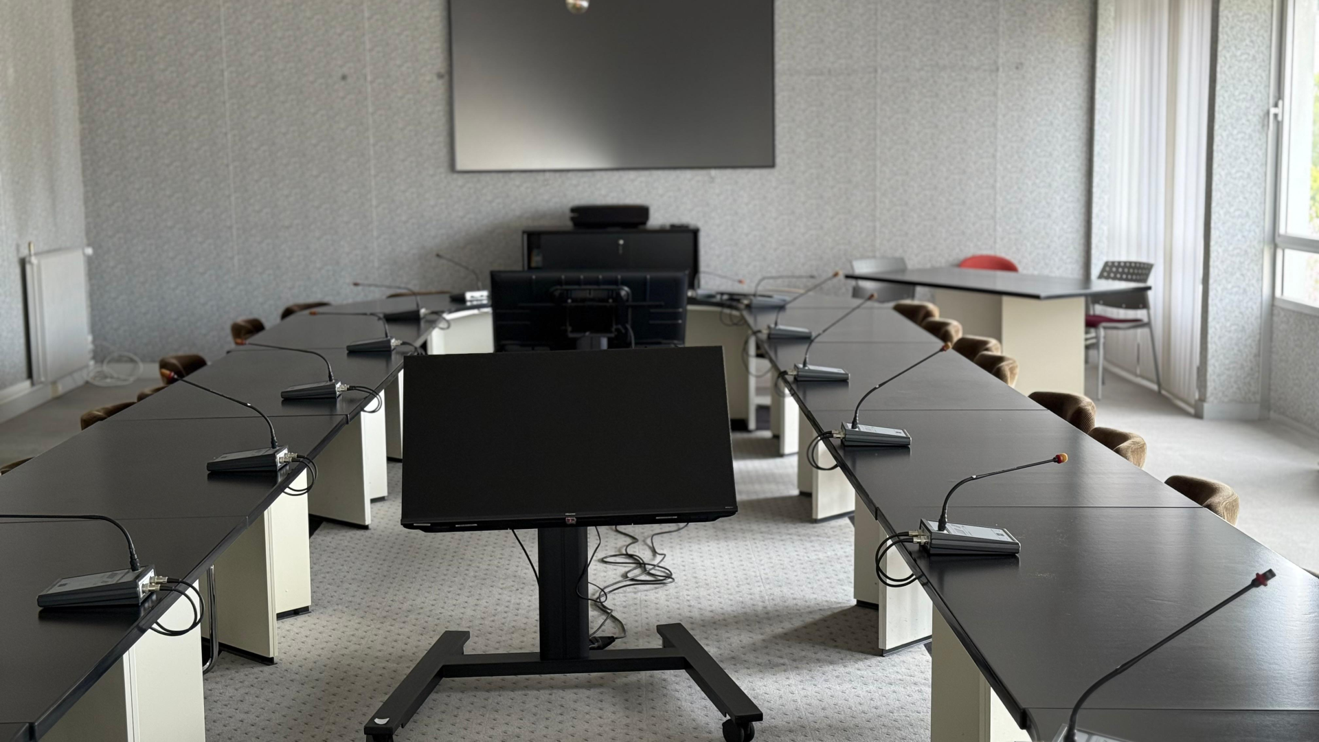 Salle de réunion avec tables, chaises, écrans, vidéoprojecteur et ordinateurs.