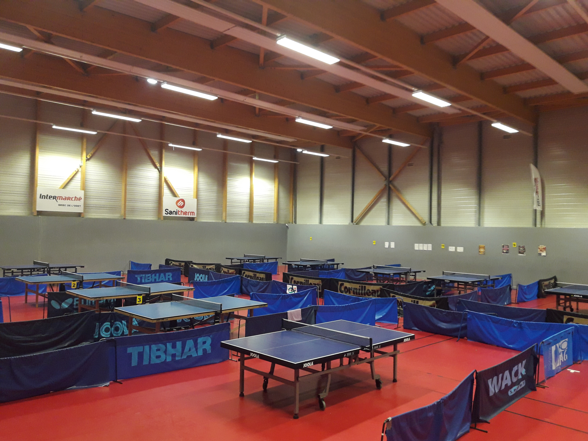 Salle de sport avec tables de ping-pong, filets et raquettes.