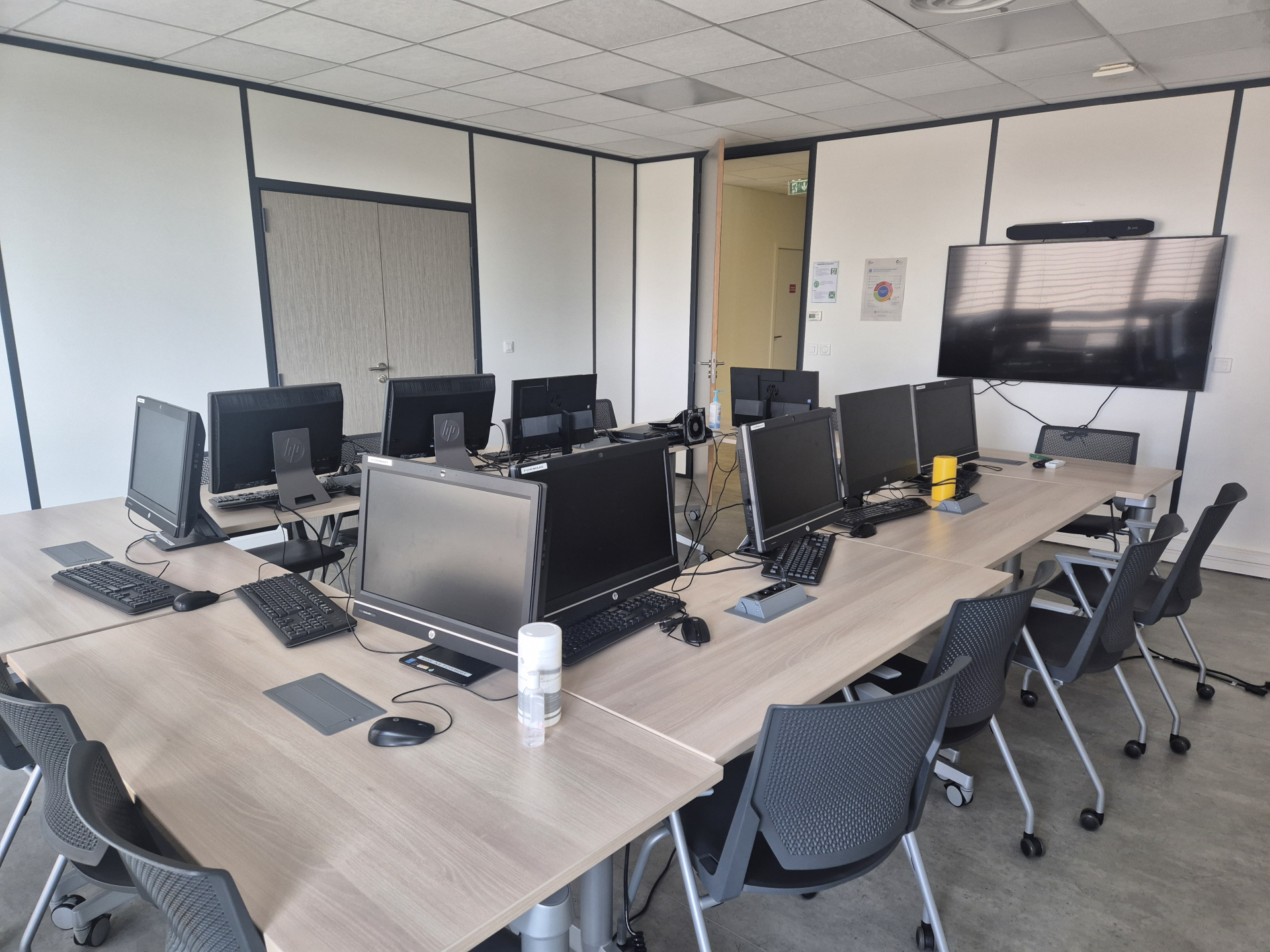Salle avec table, chaises, écran, ordinateurs et claviers.