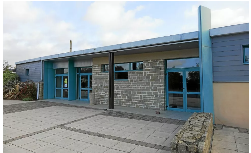 Bâtiment avec murs en brique, portes bleues, et toiture plate. Pavage devant l'entrée.