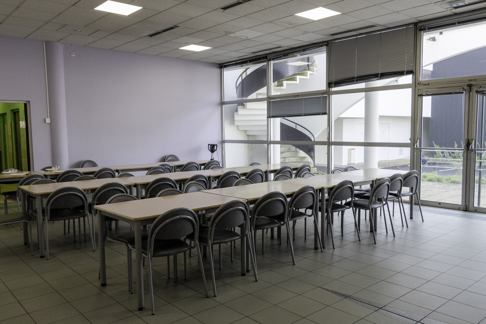 Salle avec tables, chaises, et fenêtres vitrées.