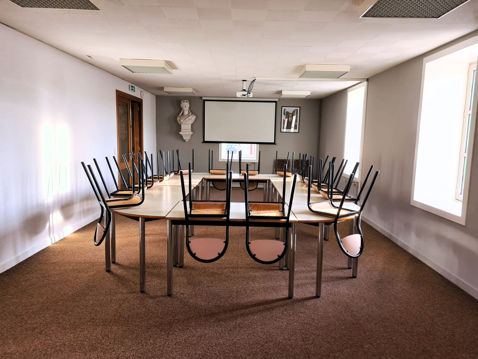 Salle avec table, chaises, écran, vidéo projecteur et buste.