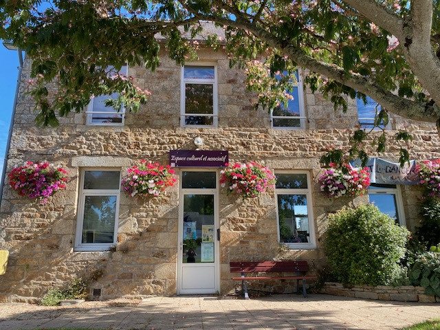 Maison en pierre avec porte d'entrée, fenêtres, fleurs suspendues, banc et arbre.