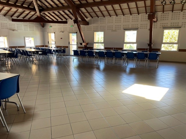 Salle avec tables, chaises, fenêtres et lumière naturelle.