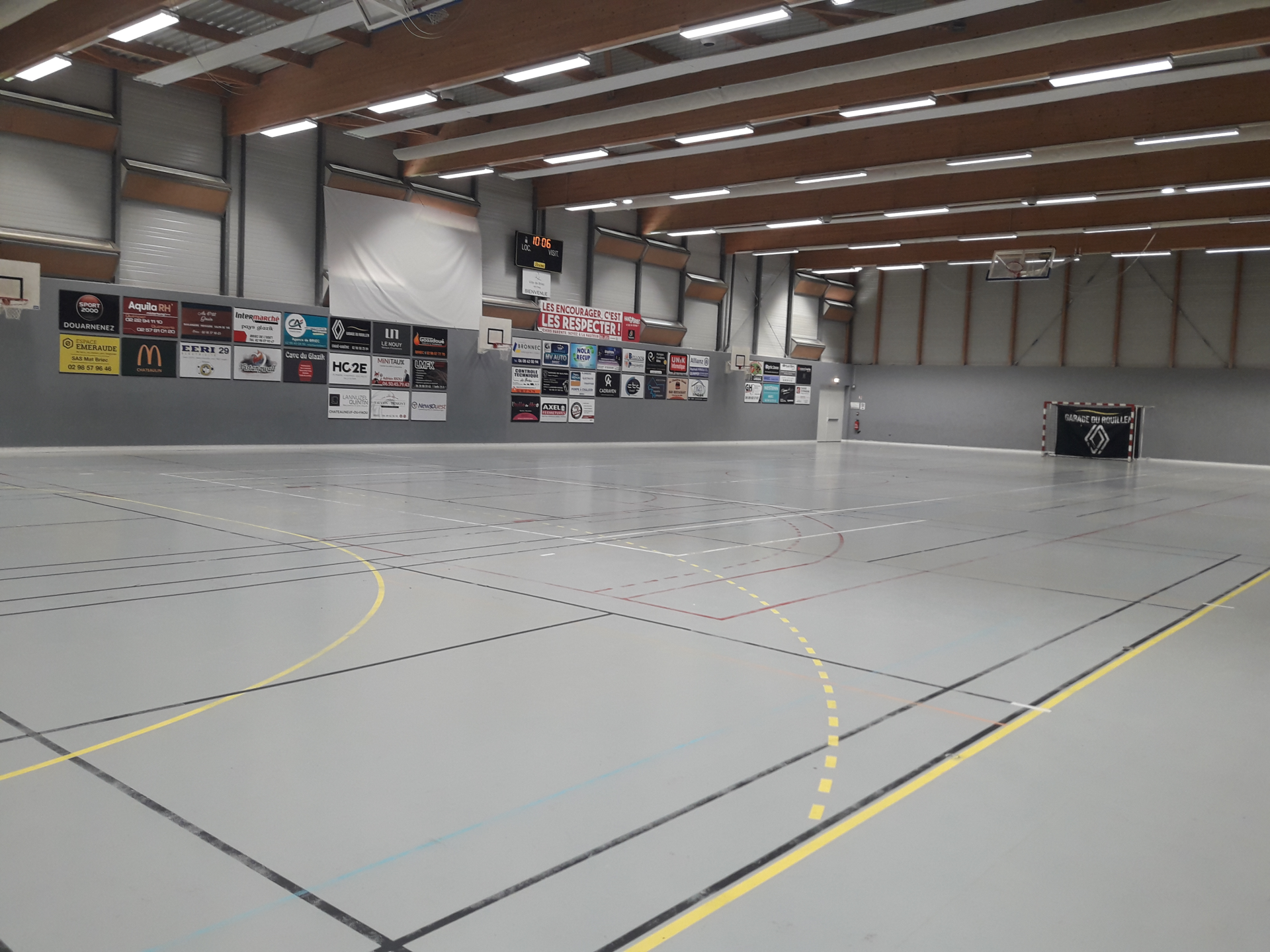 Salle de sport avec panier de basket, filet de handball, panneaux publicitaires et éclairage.