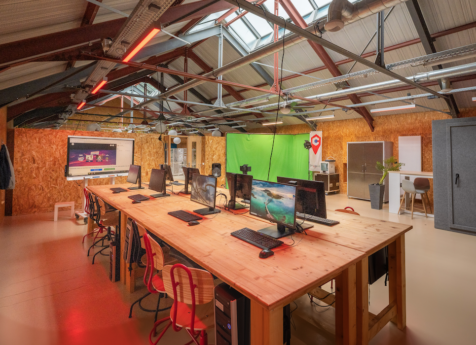 Bureau avec table, chaises, écrans, clavier et souris. Mur en bois et plafond industriel.