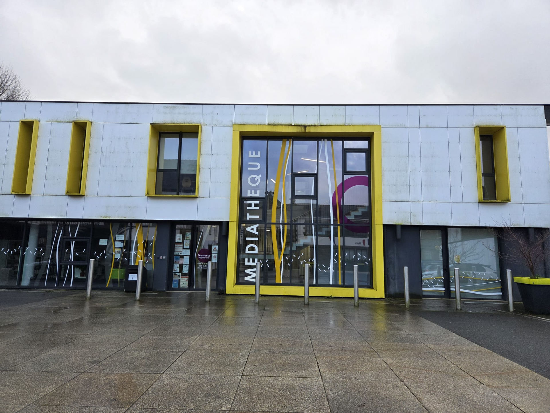 Bâtiment avec façade blanche et jaune, grandes vitres, entrée principale marquée "Médiathèque".