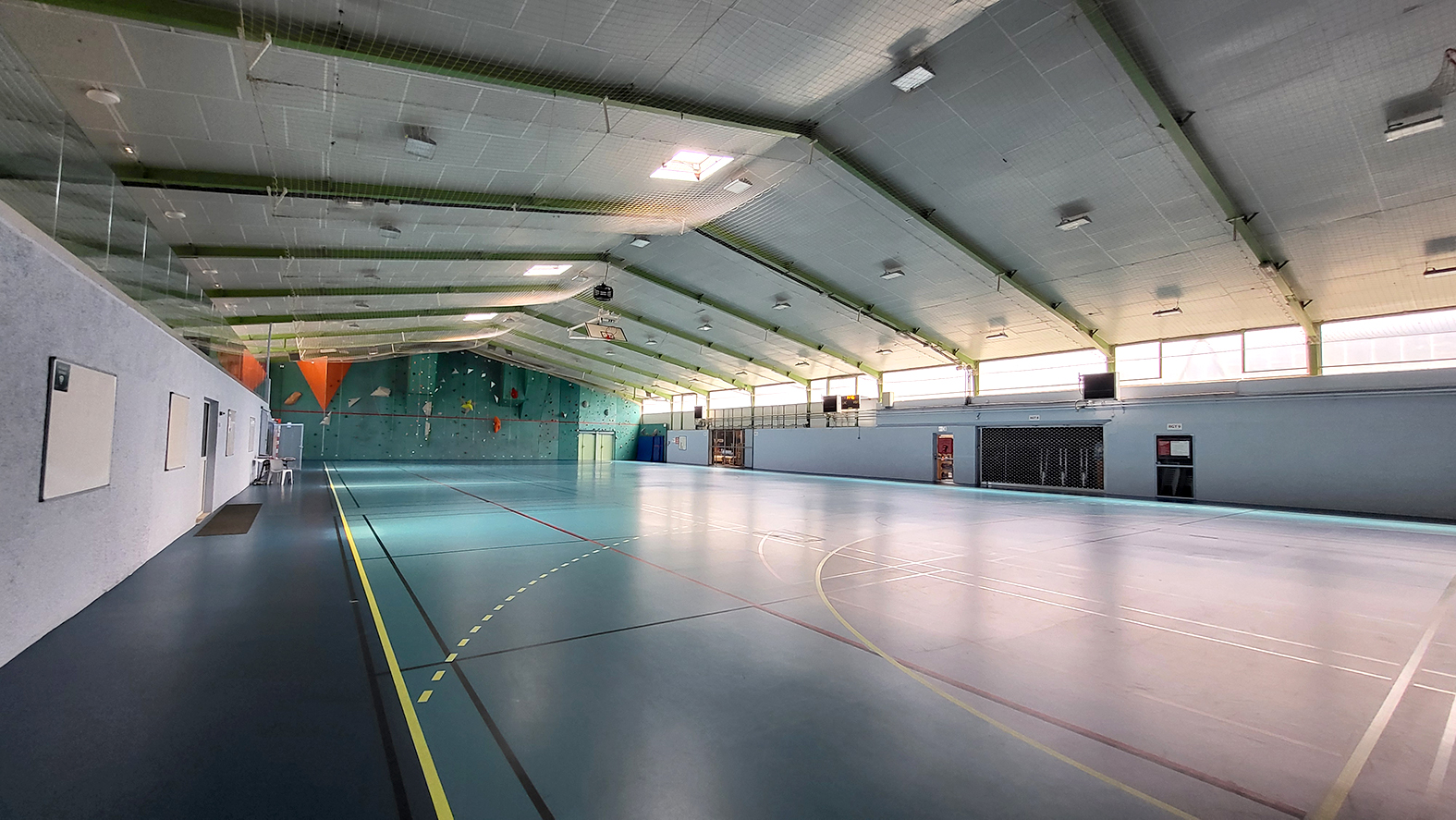 Salle de sport avec paniers de basket, murs d'escalade et éclairage.