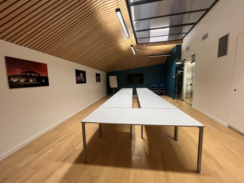 Salle avec tables, écran, tableau blanc, chaises, et peintures murales.
