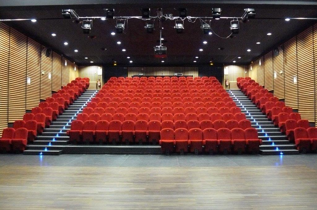 Salle de spectacle avec sièges rouges, scène, éclairages suspendus et parois acoustiques.