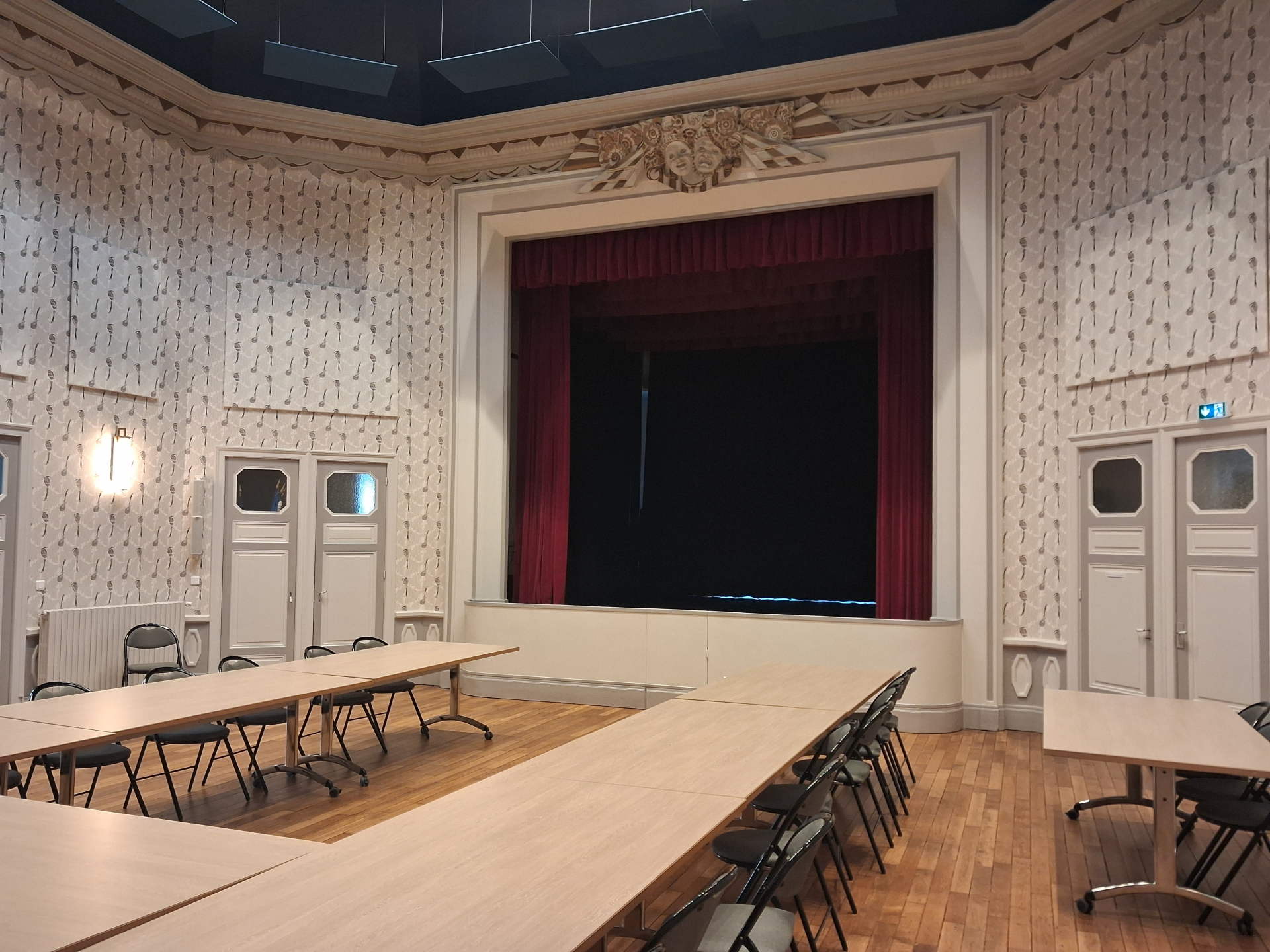 Salle avec tables, chaises, rideau de scène, portes et rampes d'accès.