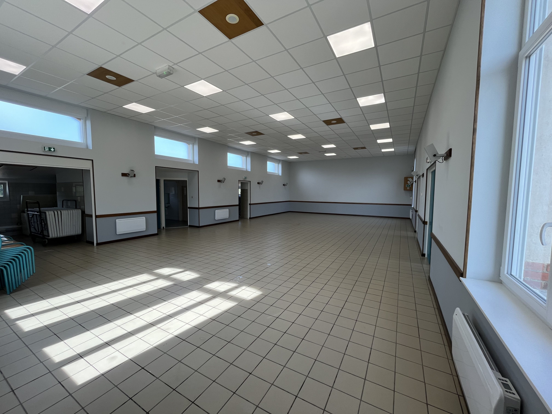 Salle vide avec carrelage, fenêtres, portes, radiateurs et éclairage au plafond.