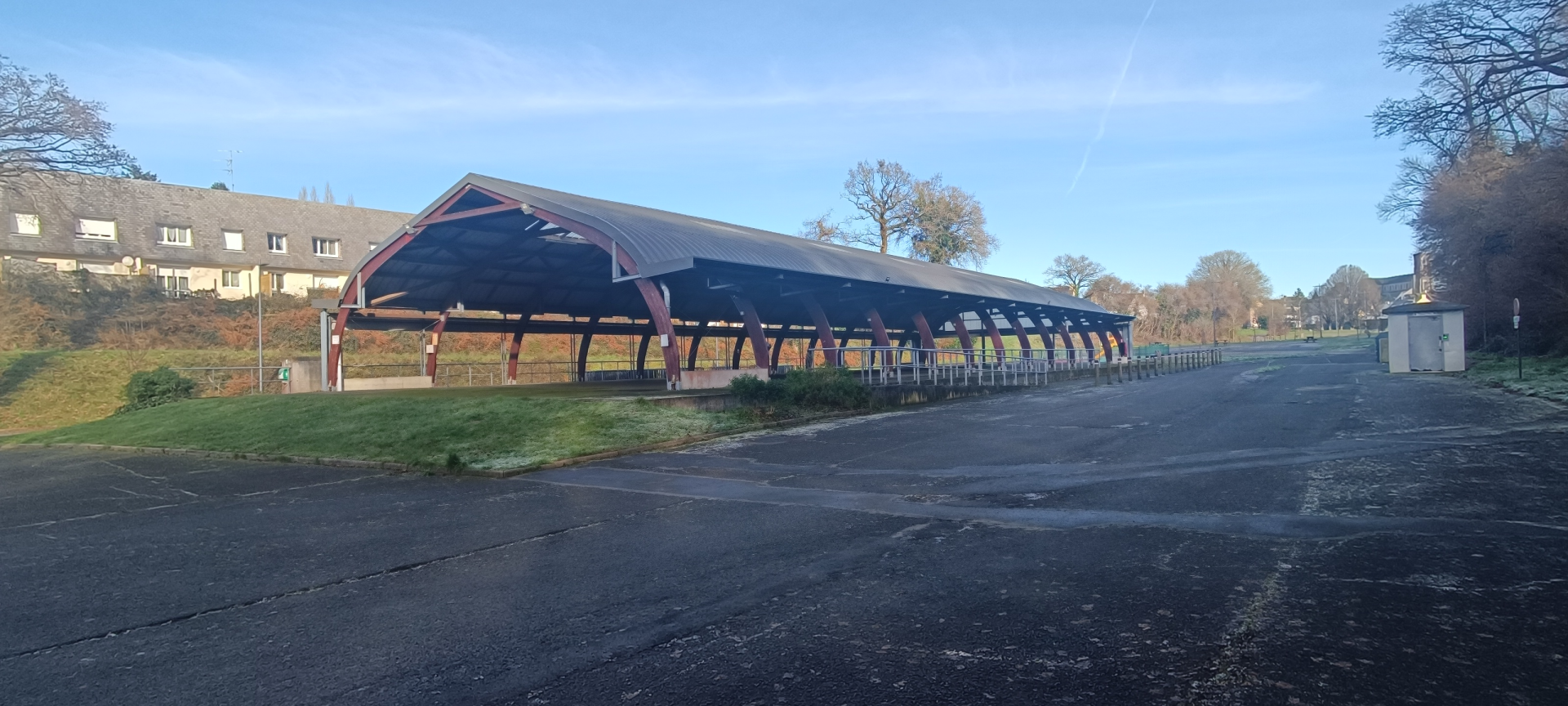 Structure couverte avec bancs et bâtiment en arrière-plan.