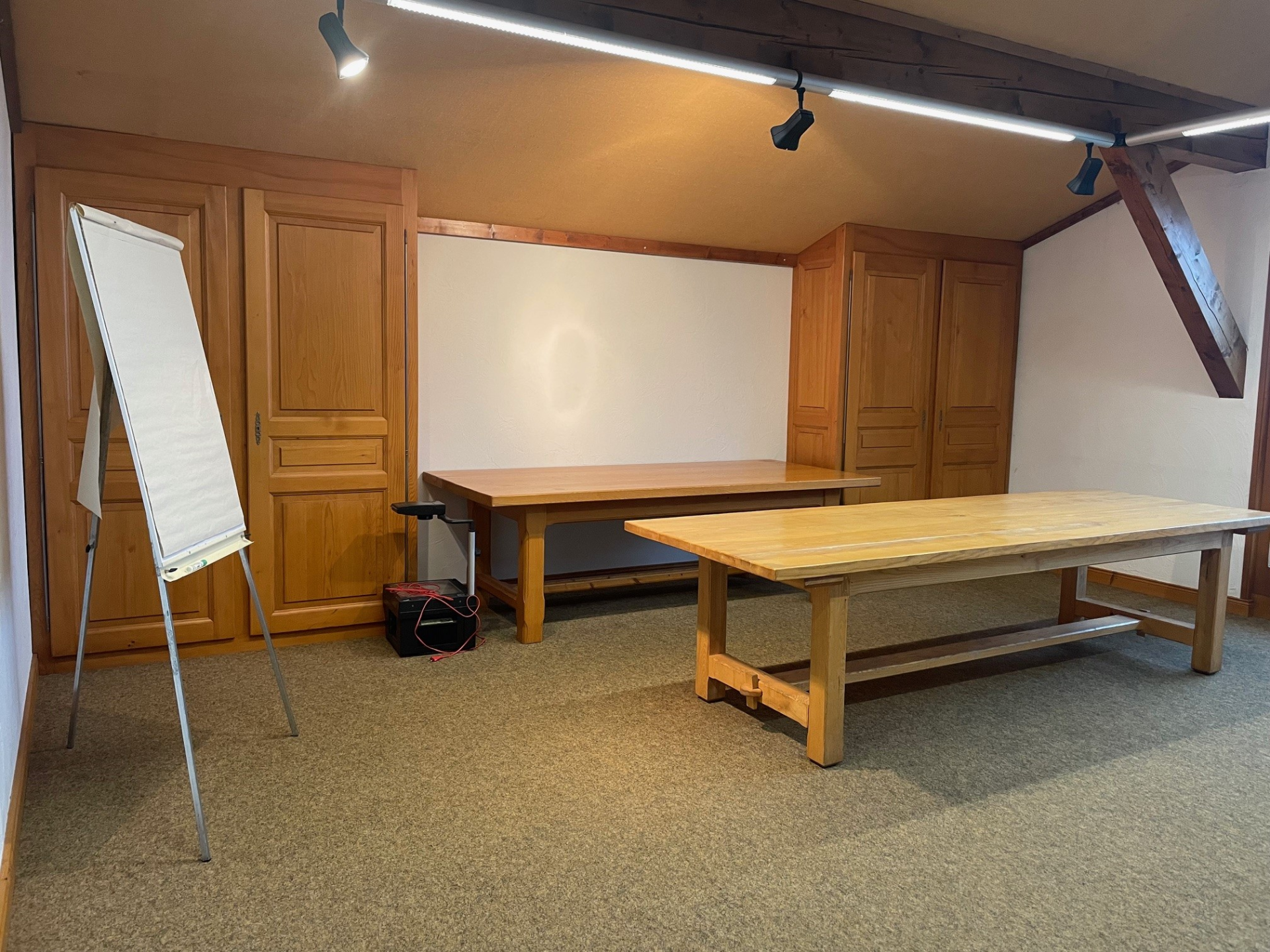Salle de réunion avec tableau, deux tables, et armoires.