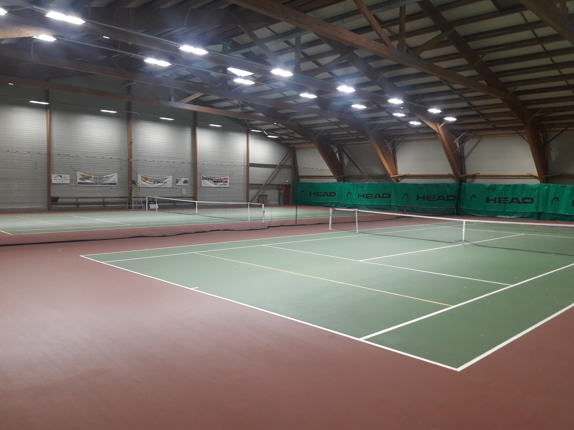 Terrain de tennis intérieur avec filets, éclairage et publicités murales.