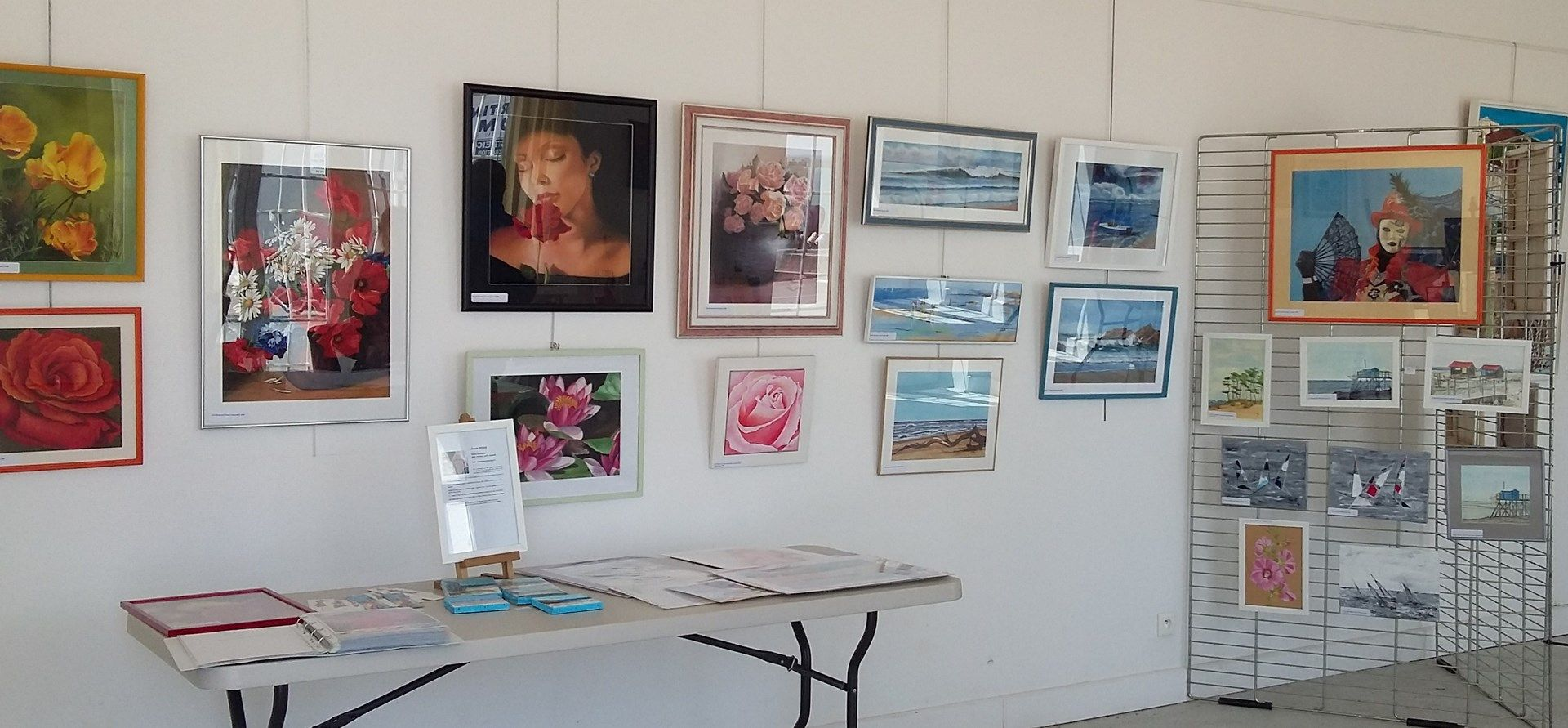 Exposition avec tableaux, cartes postales et brochures sur table.
