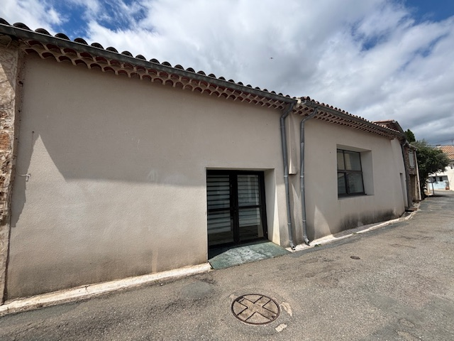 Maison avec toiture de tuiles, porte et fenêtre. Rue pavée avec regard.