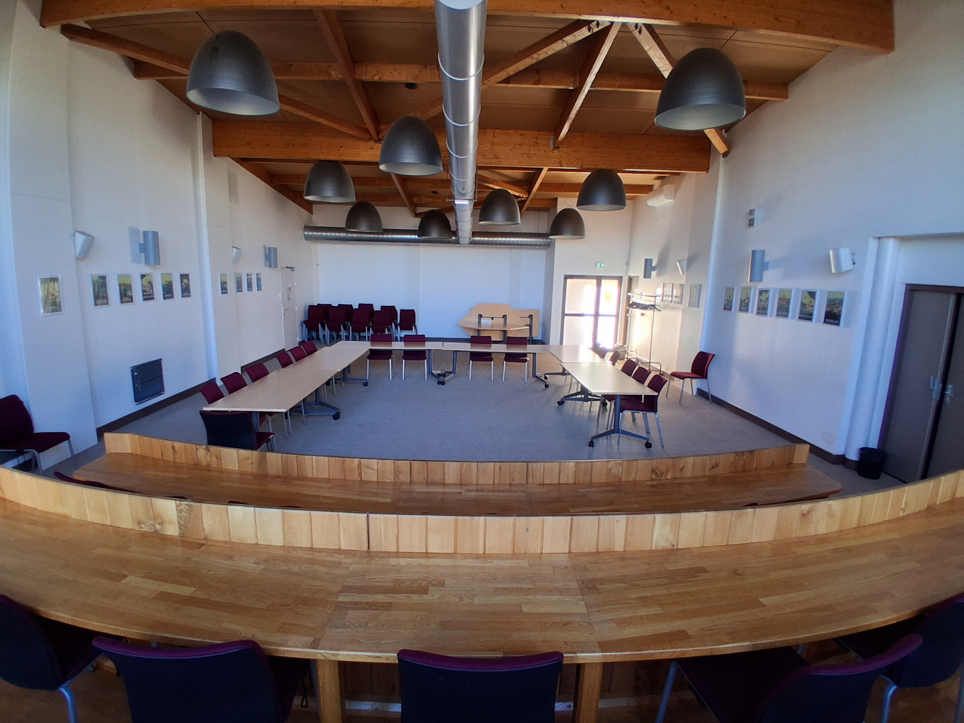 Salle avec tables, chaises, luminaires suspendus, tableaux et porte.