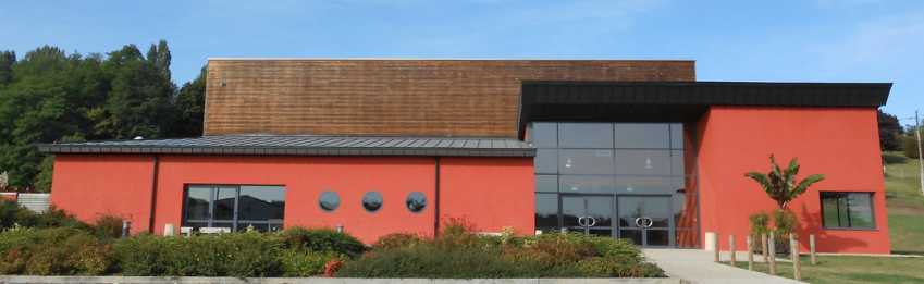 Bâtiment rouge moderne avec toiture en bois, grande façade vitrée, végétation devant.