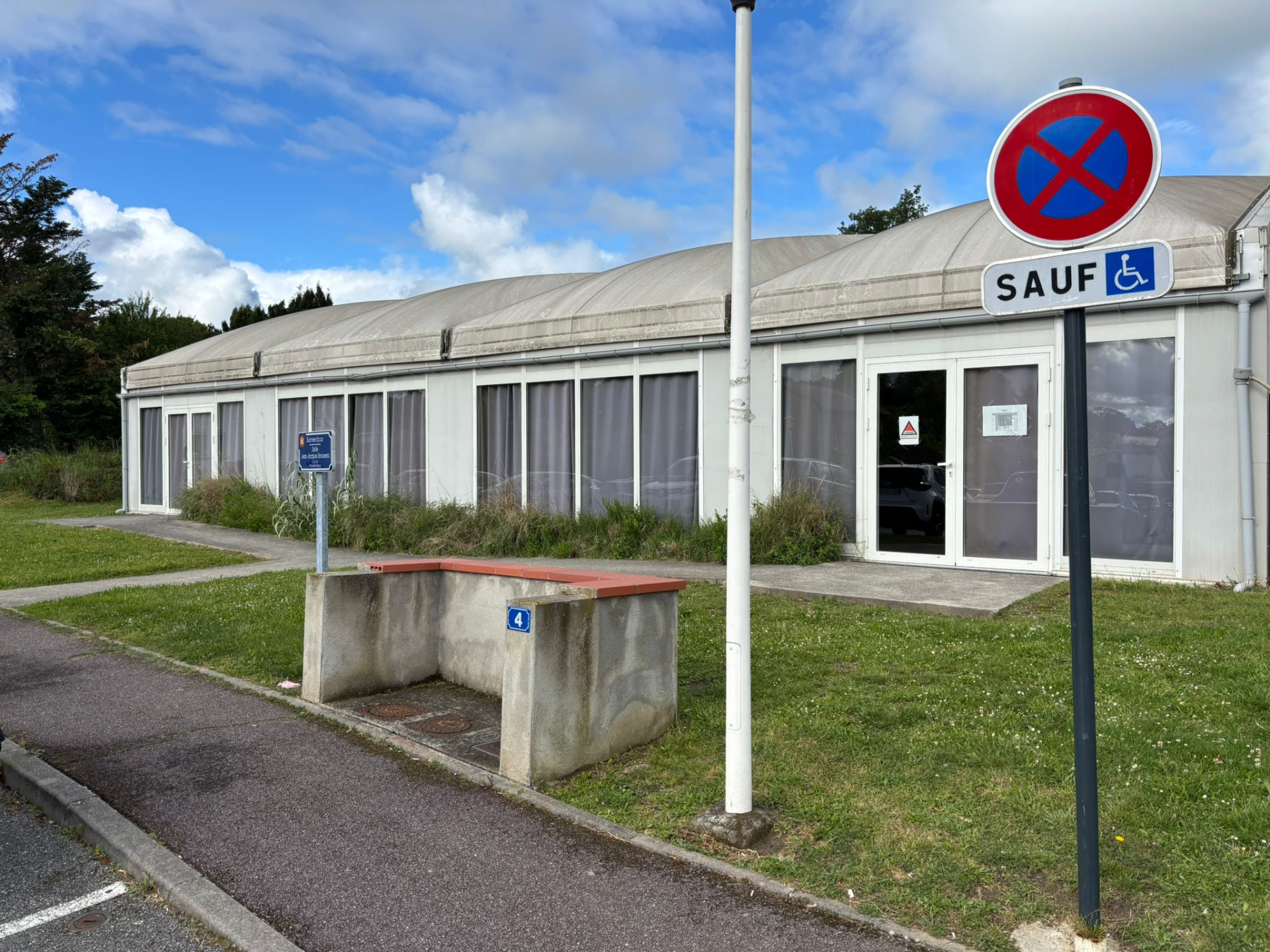 Bâtiment avec entrée, banc, panneau d'interdiction de stationner et panneau d'accessibilité.