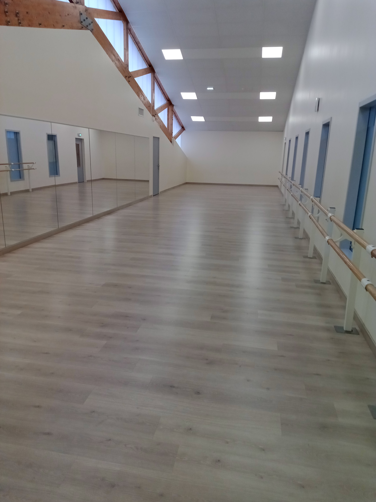 Salle spacieuse avec plancher en bois, miroirs et barres.