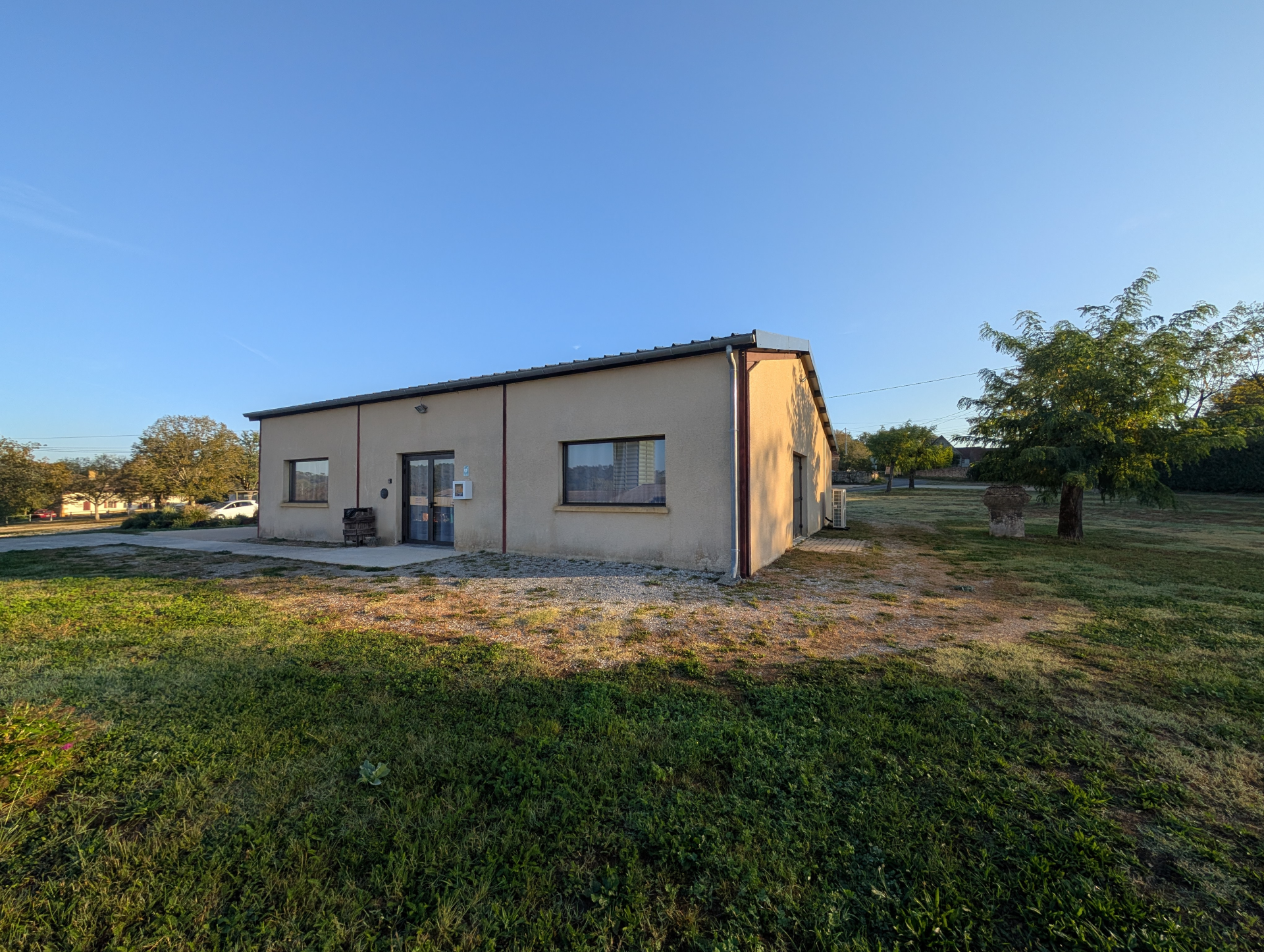 Bâtiment bas avec porte et fenêtres, situé dans une zone herbeuse.