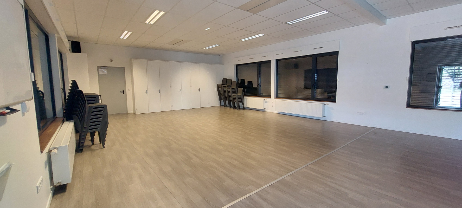 Salle vide avec chaises, portes, fenêtres et radiateurs.