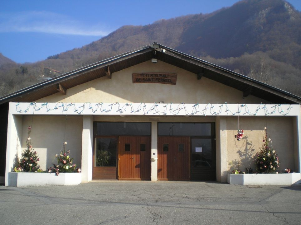 Bâtiment avec porte en bois double, porte plus petite, décorations florales, enseigne, montagnes en arrière-plan.