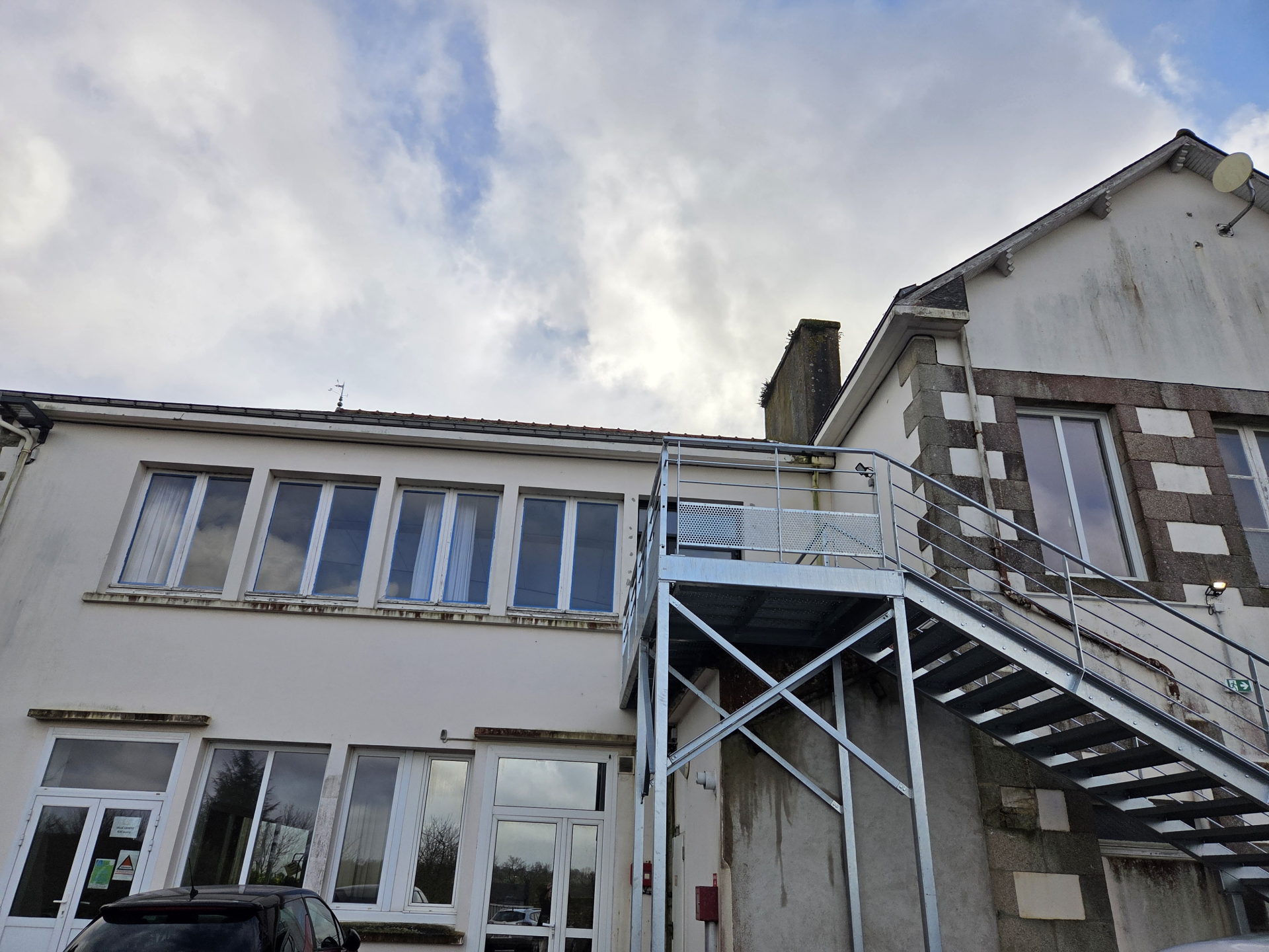 Bâtiment avec escaliers extérieurs et voitures garées.
