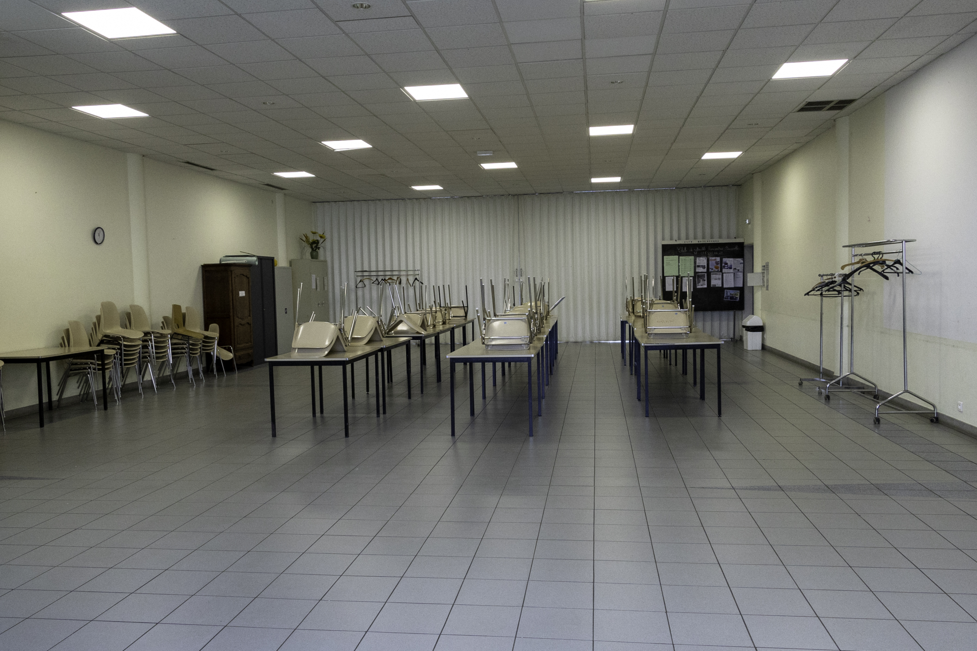 Salle de classe avec tables, chaises, projecteurs, armoire et supports pour vêtement.