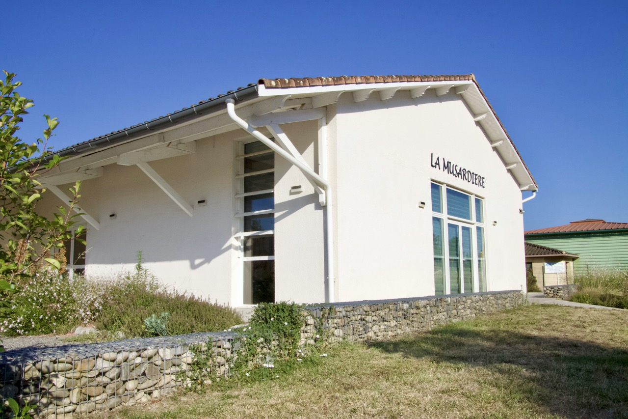 Bâtiment blanc avec toit rouge, grandes fenêtres, murs en pierre, jardin sec.