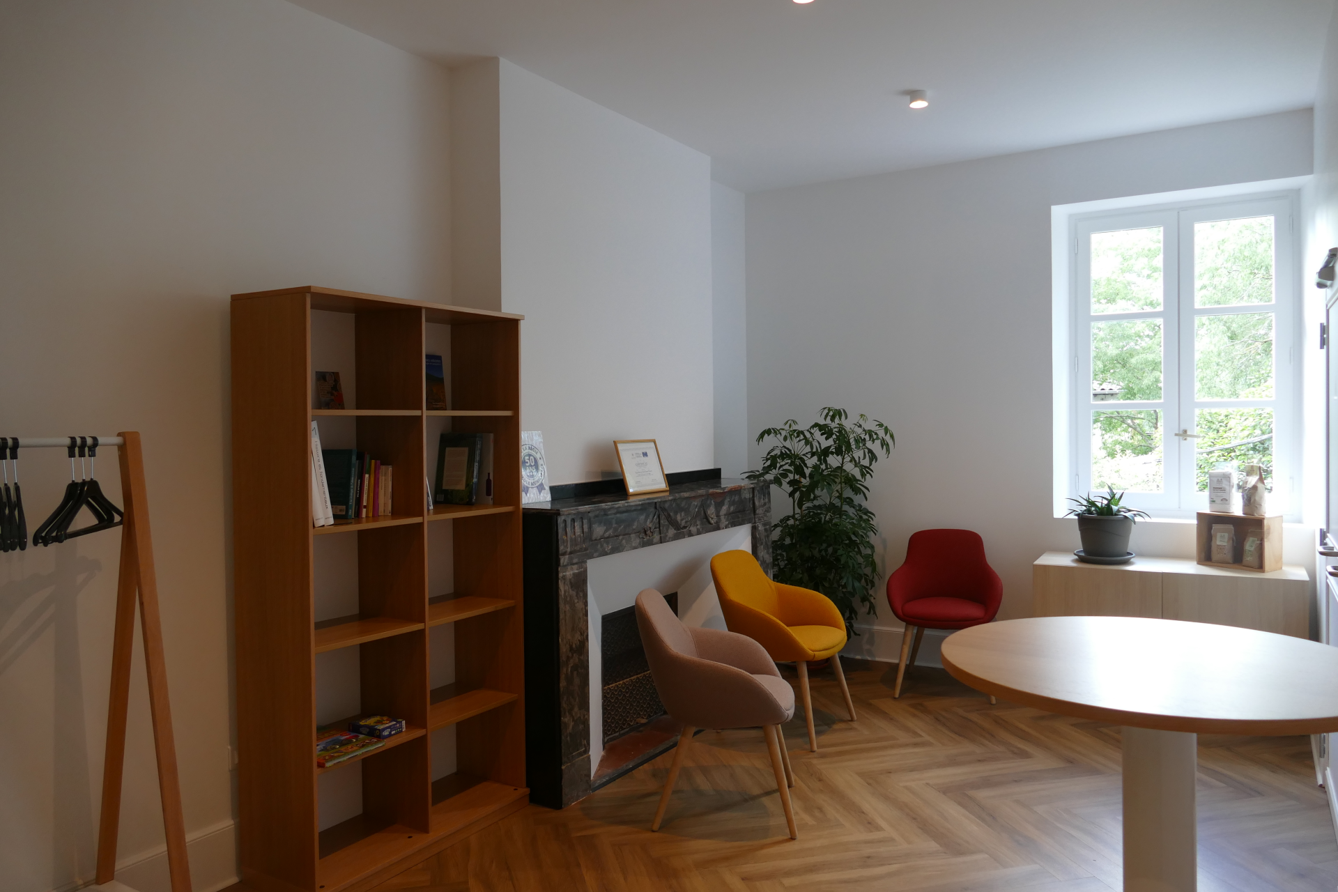Pièce avec étagères, chaises, table ronde, plantes, cheminée et porte-manteau.