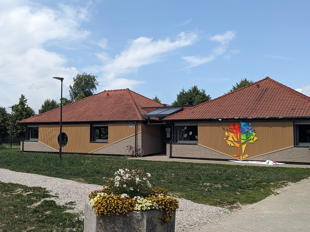 Bâtiment avec toits rouges, murs en bois, panneaux solaires, graffiti, vélo, réverbère, fleurs.