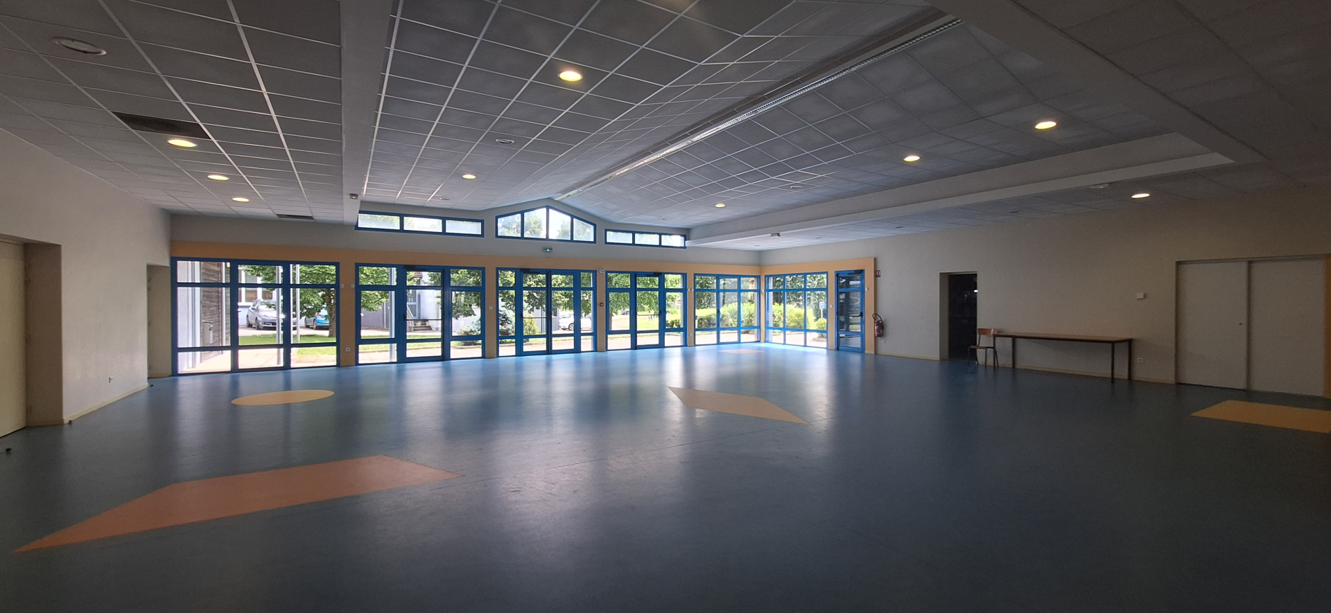 Salle vide avec grandes fenêtres, portes et taches au sol.