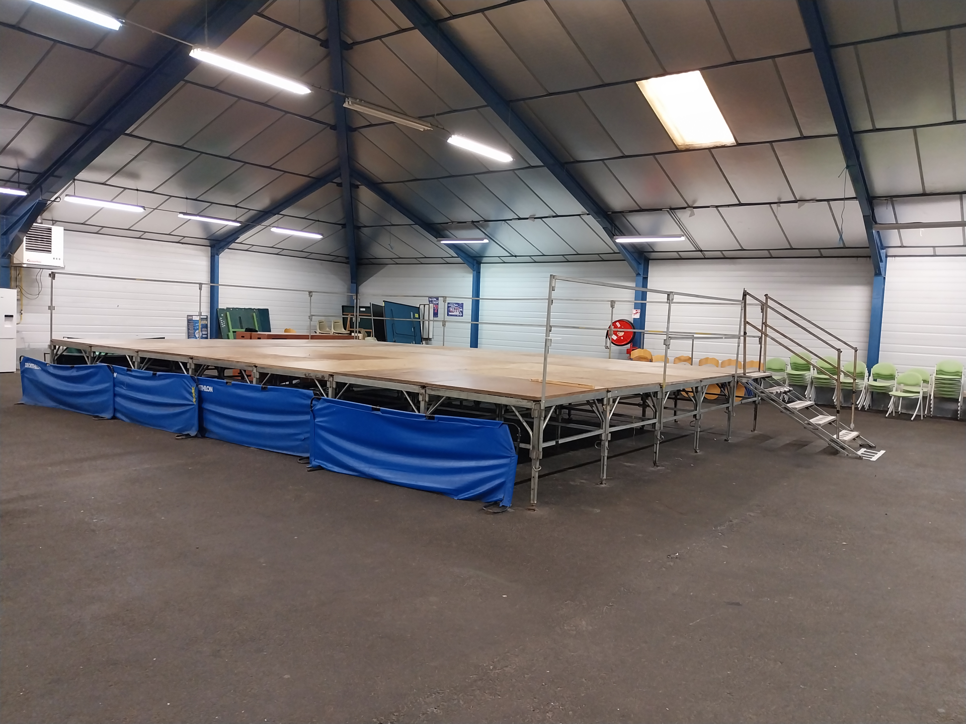 Salle avec scène, escaliers, chaises, et éclairage.