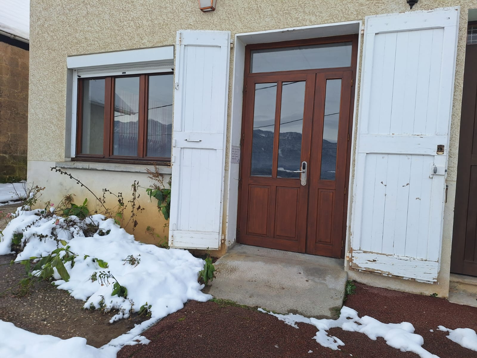Maison avec porte en bois et fenêtres, neige au sol.